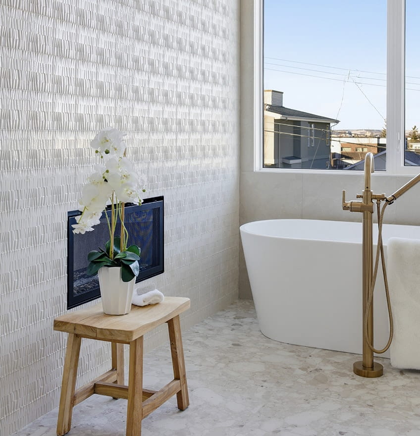 Gray tiled shower with a built-in bench, rolled towel, wooden brush, and green leaves. Chevron pattern tiles add a sleek, modern feel.
