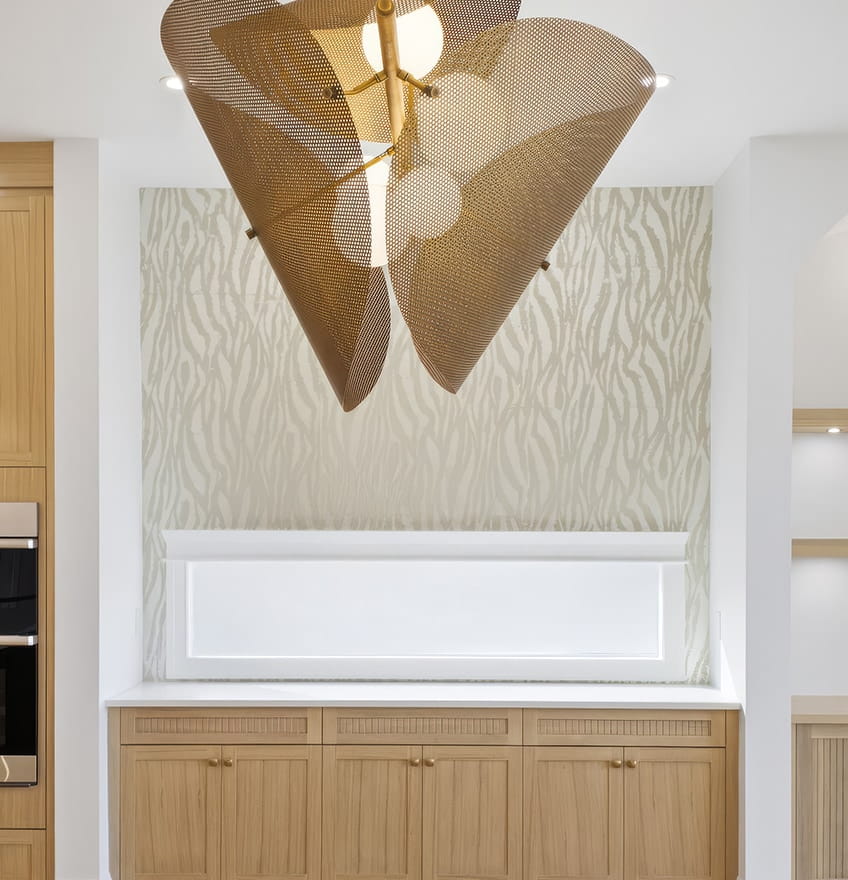 A modern kitchen with light wooden cabinets and a glass door with black hinges. The backsplash features gray tiles, and recessed shelving is lit softly.